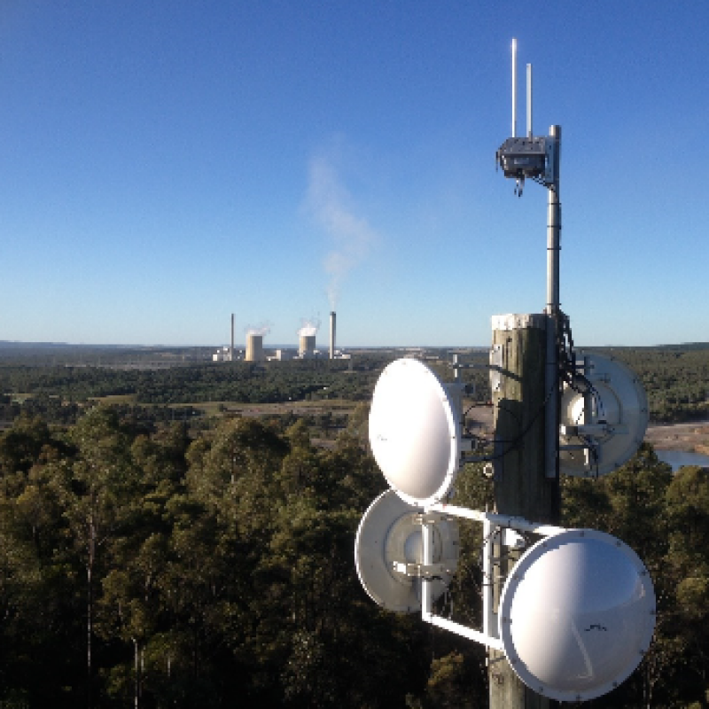 Communications Tower against blue sky with plant in distance